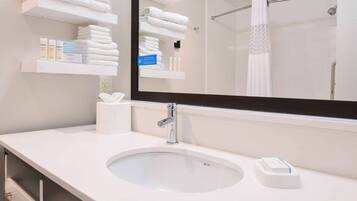 Une salle de bain moderne avec un grand miroir, un lavabo blanc et des porte-serviettes.