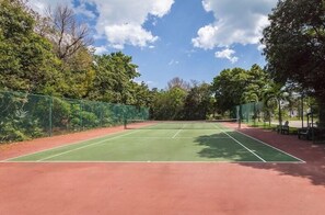 Un court de tennis aux surfaces vertes et rouges, entouré d’arbres et d’une clôture.