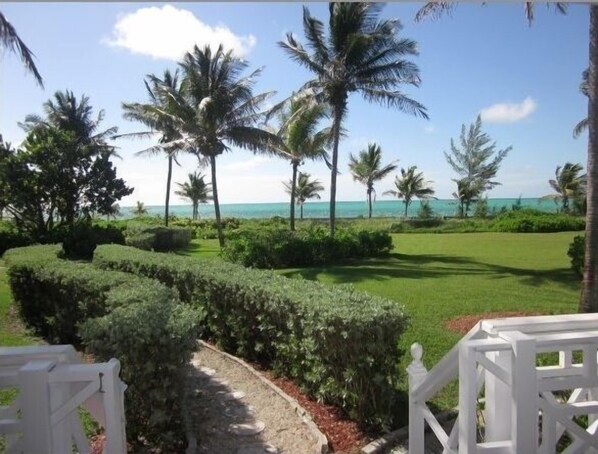 A well-maintained garden with a pathway leading to a white gate, surrounded by lush greenery and palm trees, overlooking a clear blue sky and a distant view of the ocean. - The Blue Inn Villa, 3 Bedroom Vacation Home (Freeport)