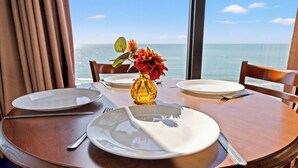 A dining table with plates, cutlery, and a vase with flowers, set against a view of the ocean. - Units at Patricia Grand Resort by Elliott Beach Rentals (Myrtle Beach)