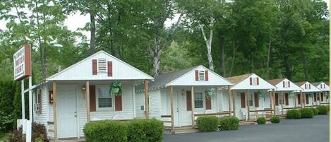 A row of white mobile homes with brown shutters, each with a porch and a small garden area in front.
