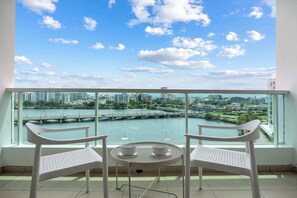 Ein Balkon mit zwei weißen Stühlen, einem runden Tisch und zwei Gläsern, mit Blick auf Stadt und Fluss.