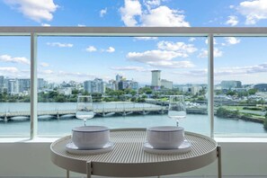 A table with two bowls and two glasses, a window with a cityscape view, and a bridge in the background. - Scenic Studio ° Lagoon Views & Sunset Balcony (San Juan)