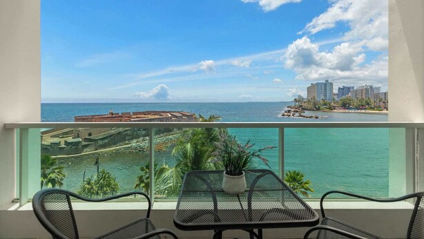 A balcony with a view of the sea, a table with a plant, and two chairs. - Scenic Studio ° Lagoon Views & Private Balcony (San Juan)