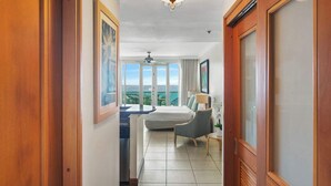 A hotel room with a bed, a chair, a desk, a ceiling fan, and large windows. - Scenic Studio ° Lagoon Views & Private Balcony (San Juan)
