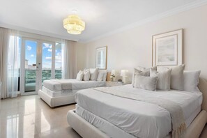 Quarto de hotel com duas camas, um candelabro, uma janela grande com vista e um quadro na parede.
