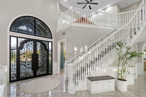 A spacious foyer with a grand staircase, a decorative glass door, and a potted plant. - 5-acre Luxe 5B Getaway @Murrieta | Pool, Hot Tub (Murrieta)