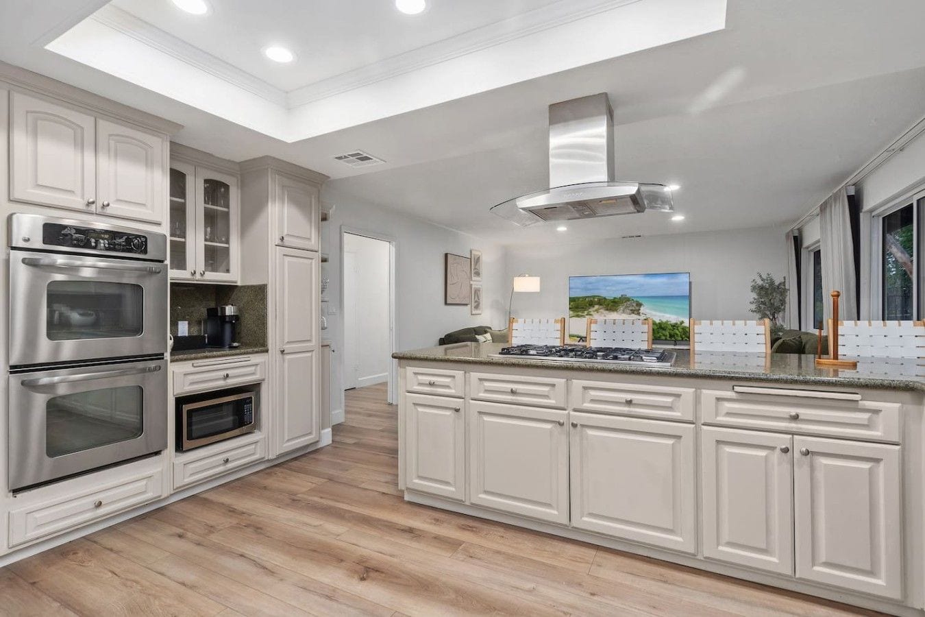 A modern kitchen with white cabinetry, stainless steel appliances, and a skylight.