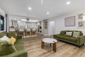 Una sala de estar moderna con un sofá verde, una mesa de centro redonda y un comedor con cocina al fondo.
