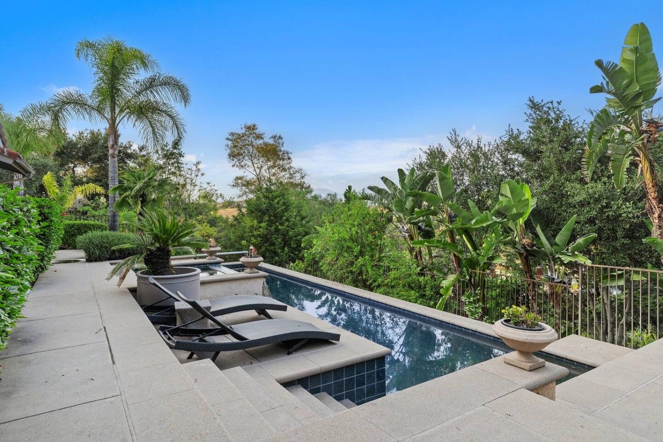 A pool area with lounge chairs, a water feature, and lush greenery.