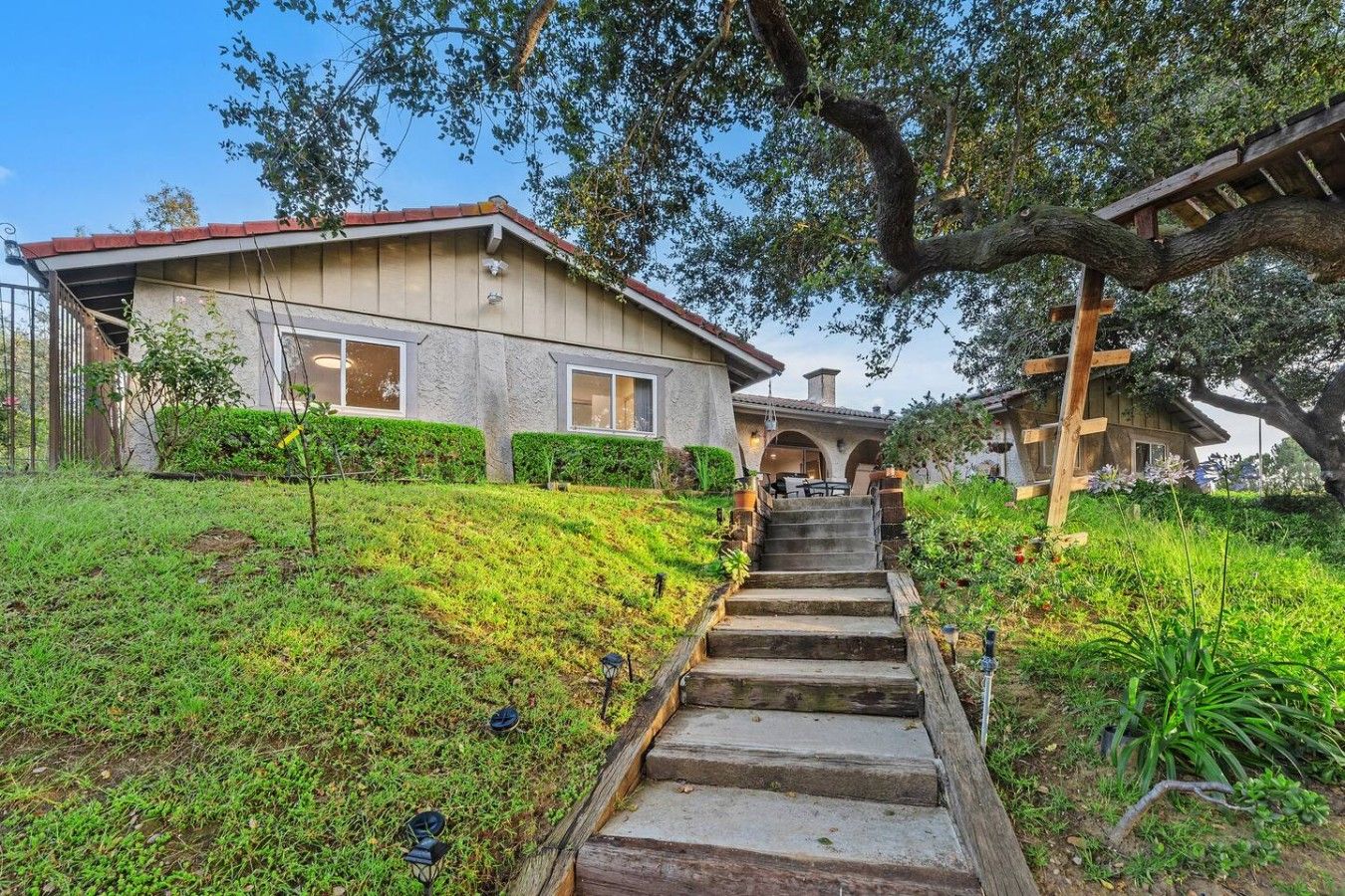 A house with a stone facade, a wooden staircase leading to a covered porch, and a garden with a variety of plants.