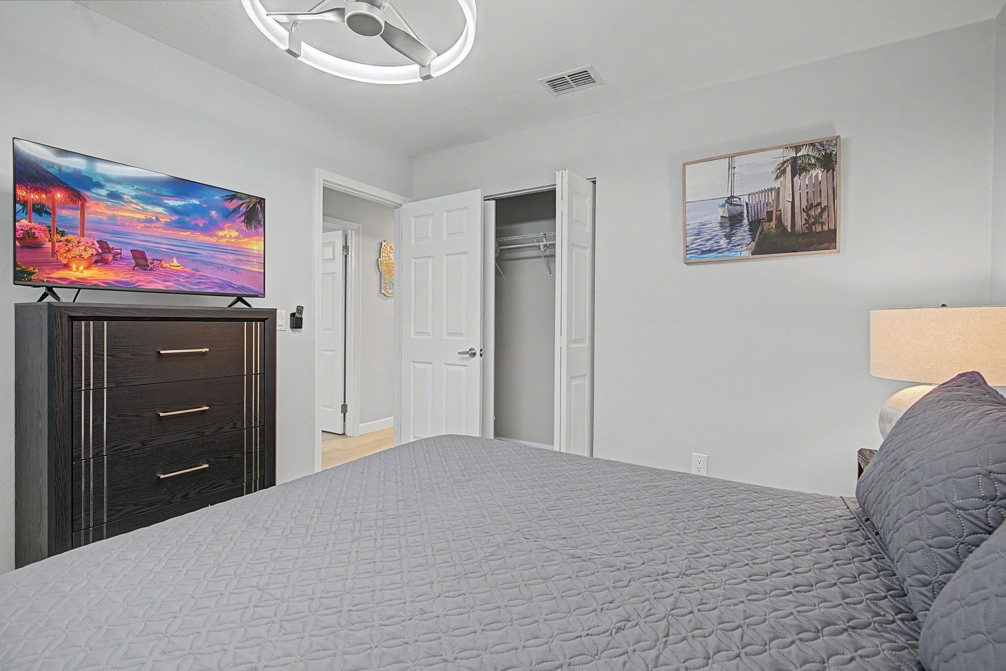 A bedroom with a bed, a TV on a stand, a wardrobe, and a door leading to another room.