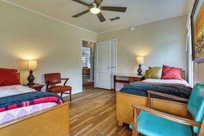 A hotel room with a bed, two chairs, a desk, a ceiling fan, and a door leading to another room. - Work & Play in Fort Worth! Retro Home 5 Mi to TCU (Fort Worth)