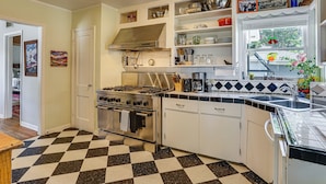 A kitchen with a checkered floor, stainless steel appliances, white cabinets, and a window with a view of greenery. - Work & Play in Fort Worth! Retro Home 5 Mi to TCU (Fort Worth)