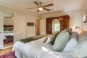 A bedroom with a bed, a ceiling fan, a mirror, and a door leading to another room. - Work & Play in Fort Worth! Retro Home 5 Mi to TCU (Fort Worth)