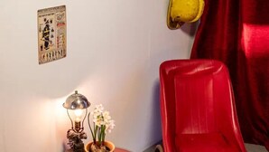 A room with a red chair, a small table with a lamp and flowers, a wall-mounted steering wheel, and a red curtain. - Cabin Sleeps 2 With Pets Welcome (Skegness)