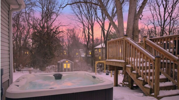 Un bain à remous dans un espace extérieur enneigé, avec une terrasse en bois et une maison en arrière-plan.