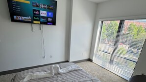 Un dormitorio con cama, televisor montado en la pared, ventilador de techo y ventana con persianas.