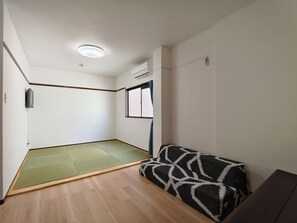 Ein Zimmer mit Tatami-Böden, einem Futon, einer Deckenleuchte und einem Fenster.