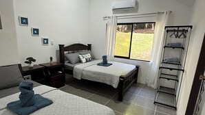Ein Schlafzimmer mit zwei Betten, einem Nachttisch, einer Kommode, einem Fenster mit Blick und einem Wäscheständer aus Metall.