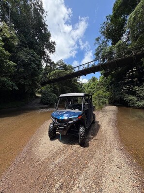 A vehicle on a gravel path under a bridge in a forested area.