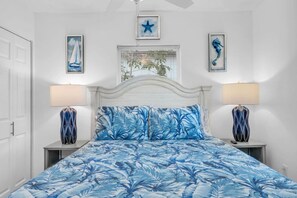 A bedroom with a bed, two nightstands, a window with blinds, and wall art.