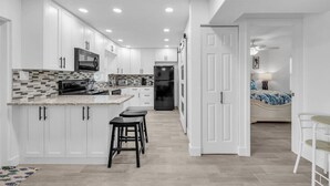 A modern kitchen with white cabinets, a central island with stools, a refrigerator, and a microwave. - Cozy Melbourne Retreat | Eau Gallie Arts | Wi-Fi (Melbourne)