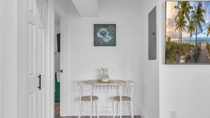 A small dining area with a table and two chairs, a painting above the table, and a beach scene painting on the wall. - Cozy Melbourne Retreat | Eau Gallie Arts | Wi-Fi (Melbourne)