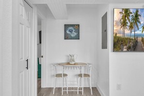 A small dining area with a table and two chairs, a painting above the table, and a beach scene painting on the wall.