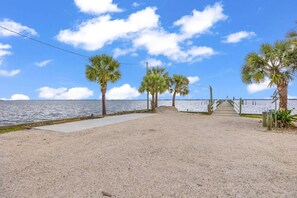 A sandy beach with palm trees, a concrete walkway, and a wooden pier extending into the water.