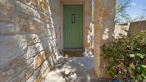 Un bâtiment en pierre avec une porte verte, une clôture en bois et un petit jardin.