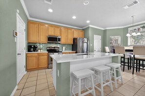 A kitchen with wooden cabinets, a stainless steel refrigerator, a microwave, and a large island with bar stools. - Spacious SA Home • Airport, Stone Oak, & Downtown (San Antonio)