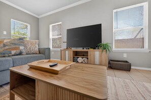 A living room with a sofa, a coffee table, a TV, and a window with blinds. - Spacious SA Home • Airport, Stone Oak, & Downtown (San Antonio)