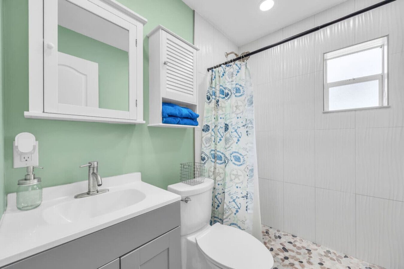 Een badkamer met een wit wastafel, spiegel en toilet. Er is een douchegordijn met een blauw patroon.
