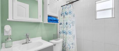 A bathroom with a white sink, mirror, and toilet. There is a shower curtain with a blue pattern.