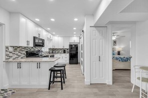 A modern kitchen with white cabinets, a central island with stools, a refrigerator, and a microwave. - Cozy Melbourne Retreat | River front | Dock | Wifi (Melbourne)