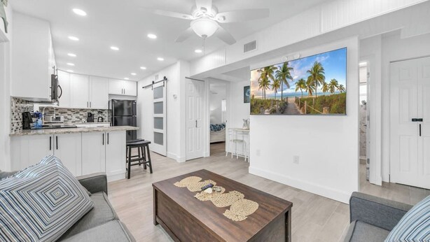 A modern kitchen with white cabinets, a dining area with a large painting, and a cozy seating area with a wooden coffee table. - Cozy Melbourne Retreat | River front | Dock | Wifi (Melbourne)
