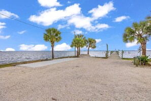 A beachside walkway with palm trees, a concrete path, and a wooden pier leading to the water. - Cozy Melbourne Retreat | River front | Dock | Wifi (Melbourne)