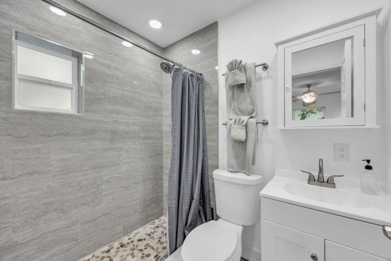 A bathroom with a shower, toilet, sink, and mirror.