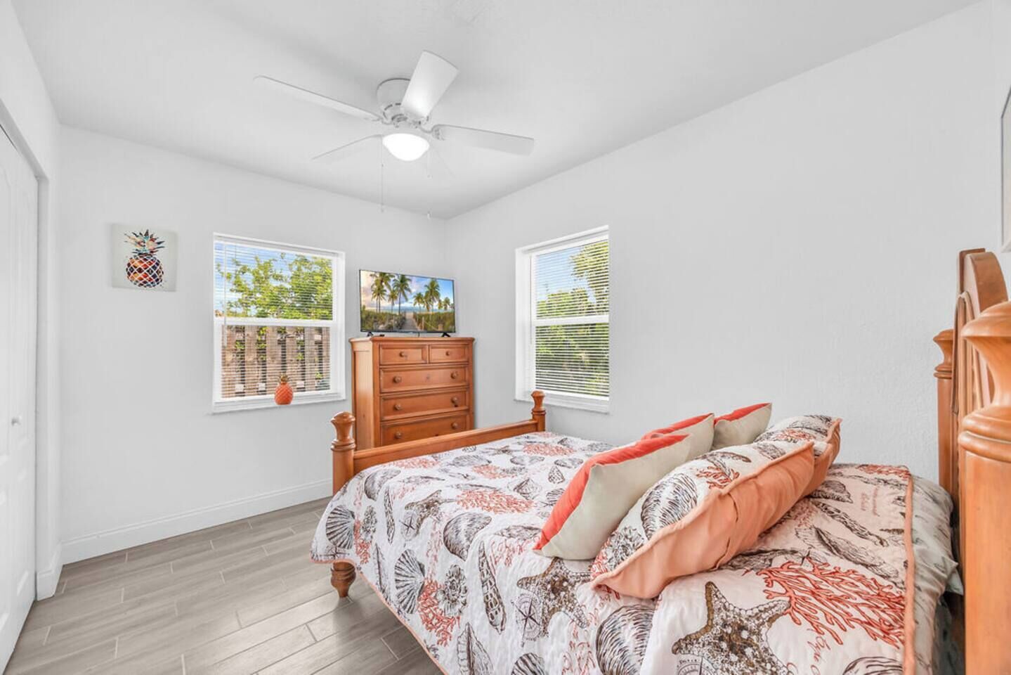 Un dormitorio con cama, cómoda, ventilador de techo y dos ventanas con persianas.