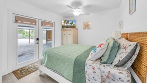 A bedroom with a bed, a ceiling fan, a door leading outside, and a small cabinet. - Cozy Melbourne Retreat | River front | Dock | Wifi (Melbourne)