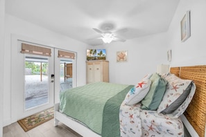 A bedroom with a bed, a ceiling fan, a door leading outside, and a small cabinet. - Cozy Melbourne Retreat | River front | Dock | Wifi (Melbourne)