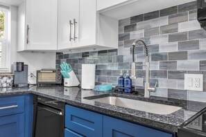 A modern kitchen with white cabinets, a granite countertop, a built-in dishwasher, and a tiled backsplash. - Cozy Melbourne Retreat | Indian river | Beaches (Melbourne)