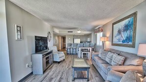 A living room with a sofa, TV, and coffee table. There is a kitchen area in the background. - Mariner’s Escape - Ocean View 3BR Sleeps 12 (Myrtle Beach)