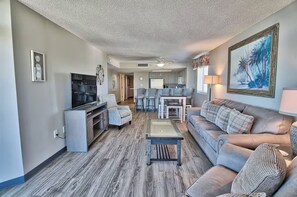 A living room with a sofa, TV, and coffee table. There is a kitchen area in the background. - Mariner’s Escape - Ocean View 3BR Sleeps 12 (Myrtle Beach)