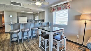 A kitchen with a central island, bar stools, a ceiling fan, and a window with blinds. - Mariner’s Escape - Ocean View 3BR Sleeps 12 (Myrtle Beach)