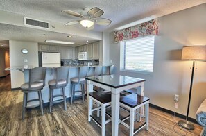 A kitchen with a central island, bar stools, a ceiling fan, and a window with blinds. - Mariner’s Escape - Ocean View 3BR Sleeps 12 (Myrtle Beach)