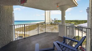 A balcony with a view of the beach and ocean, a chair, and an exit sign. - Beachfront Studio - Ocean View • Pool • Sleeps 4 (Panama City Beach)