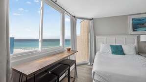 A bedroom with a large window, a bed, a desk with two chairs, and a view of the ocean. - Beachfront Studio - Ocean View • Pool • Sleeps 4 (Panama City Beach)