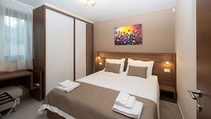 Hotellihuone, jossa on sänky, yöpöydät, työpöytä, tuoli, taulu ja kattovalaisin.